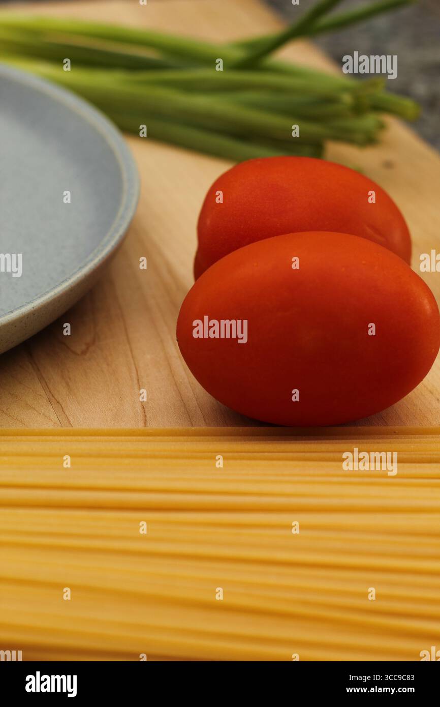 Ungekochte Pasta und frisches Gemüse auf hölzernem Schneidebrett für die Mahlzeitvorbereitung Stockfoto