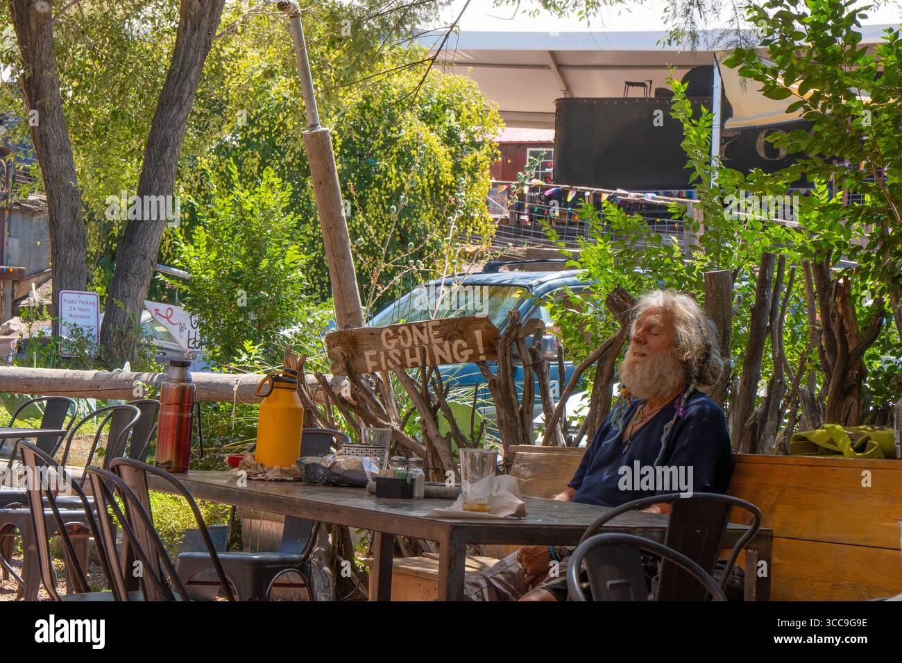 Ein älterer Mann schläft nach seinem Mittagessen neben einem Schild zum Gone Fishing, was eine humorvolle Situation in Madrid, New Mexico, schafft. Stockfoto