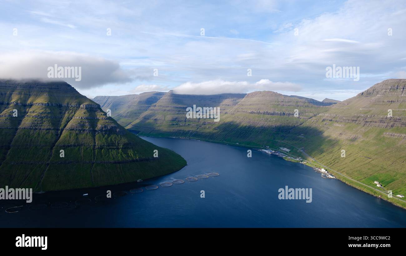 Atemberaubende Landschaft der Färöer mit steilen grünen Hügeln, die einen ruhigen Fjord umgeben. Das Sonnenlicht wirft dramatische Schatten und hebt das raue Gelände von Klakkur hervor Stockfoto