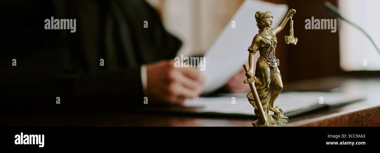 Kaukasischer Richter liest Rechtsdokumente hinter Lady Justice Statue vor Gericht Stockfoto