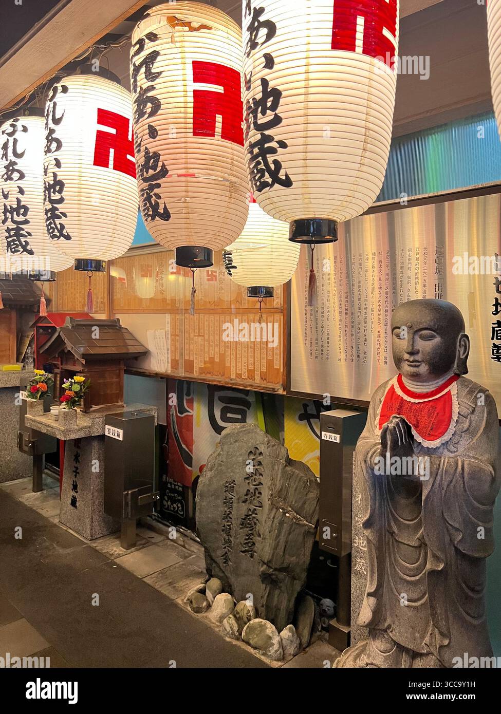 Steinstatue und Schrein mit japanischen Papierlaternen in einer warm beleuchteten Gasse, Japan. Stockfoto