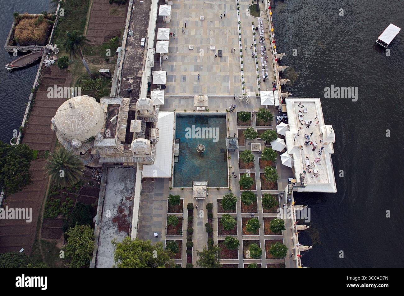 Blick aus der Vogelperspektive auf das glitzernde Lake Palace Hotel, seine Marmorfassade spiegelt das türkisfarbene Wasser wider, umgeben von gepflegten Gärten, Udaipur, Rajasthan, Indien. Stockfoto
