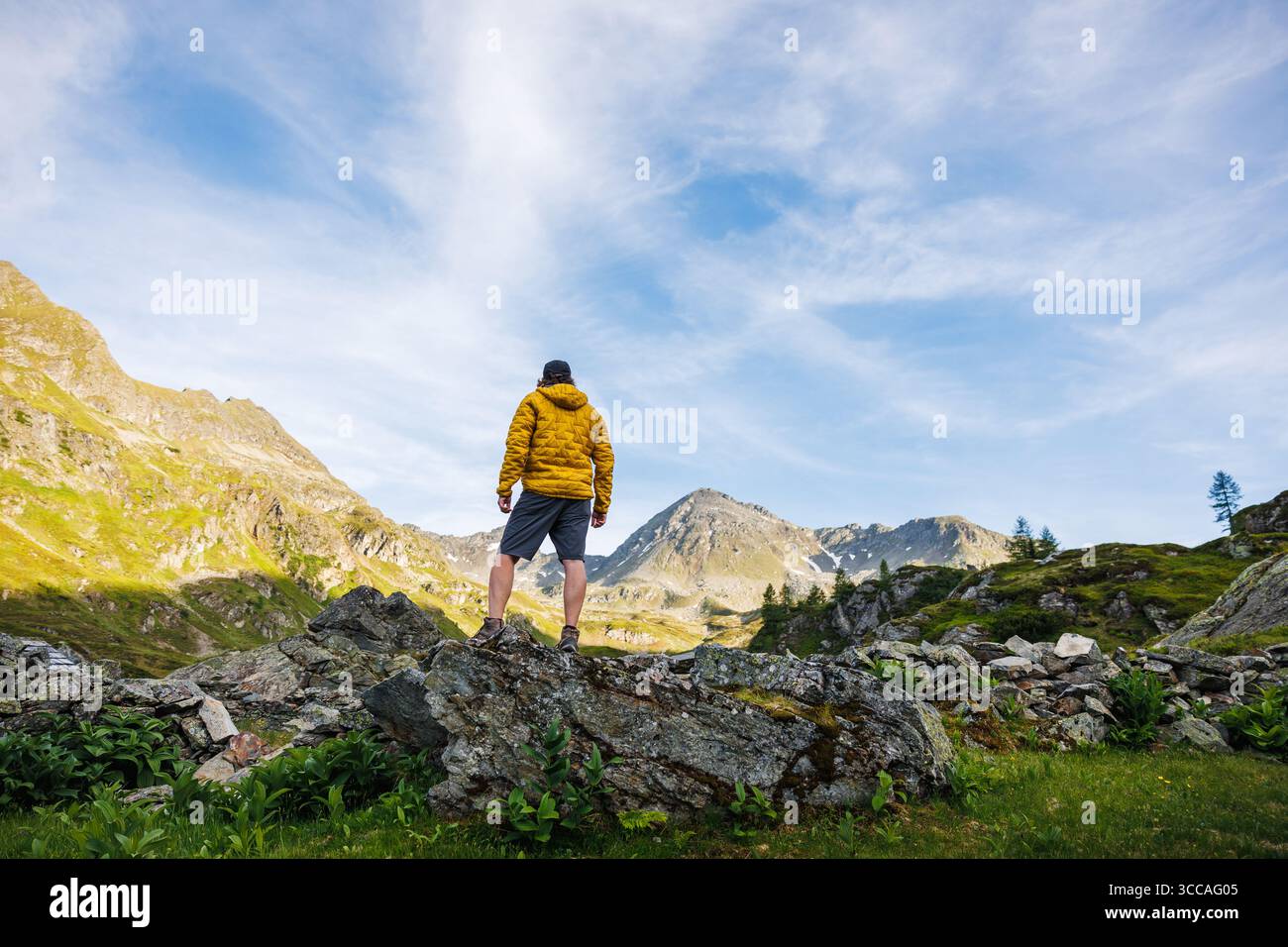 Alleinwanderer in gelber Jacke, die abgelegenes Berggelände erkunden und den Panoramablick nach einer anspruchsvollen Wanderung genießen. Outdoor-Abenteuer Stockfoto