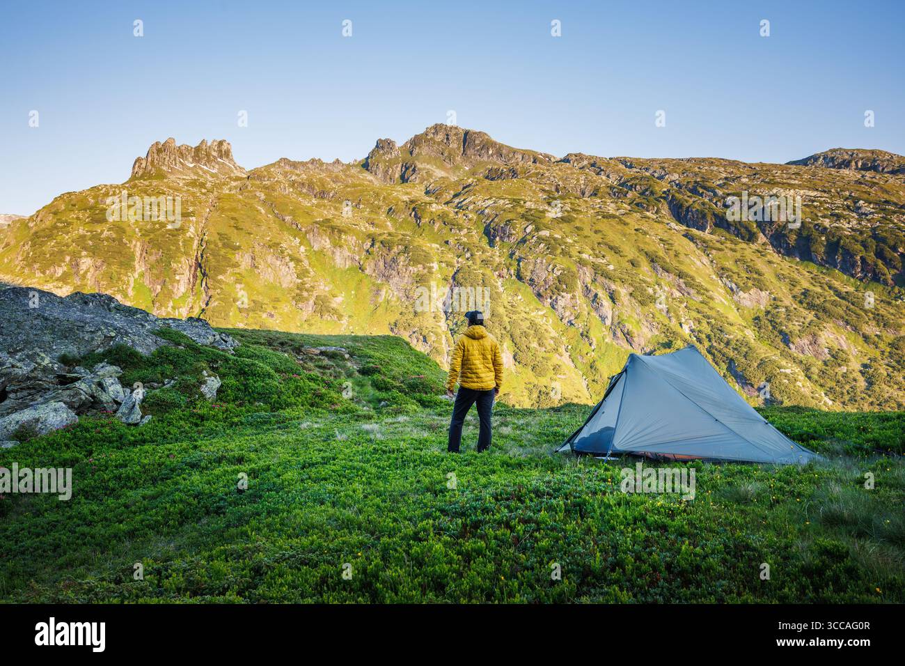 Wanderer genießt die Aussicht vom Campingplatz in den Bergen. Backpacker steht während einer langen Wanderung in den europäischen Alpen im Zelt. Wandern und Outdoor-Lifestyle Stockfoto