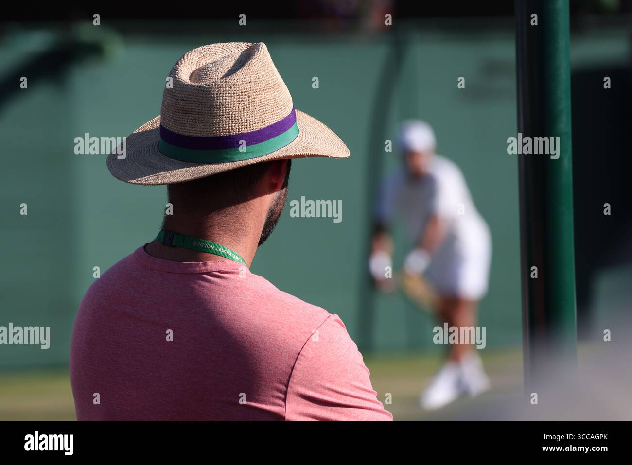 Mann mit Strohhut, der auf einem der Außenplätze sitzt und einen Spieler bei den Wimbledon Championships 2025 beobachtet, London, England, Großbritannien. Stockfoto