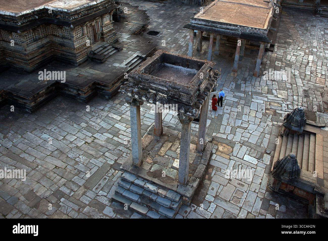 Aus der Vogelperspektive sehen Sie komplizierte Steinschnitzereien und -Strukturen, die sich nahtlos in den gepflasterten Innenhof einfügen und die architektonischen Details des Hoysaleswara Tempels, Halebidu, Karnataka, Indien, hervorheben. Stockfoto