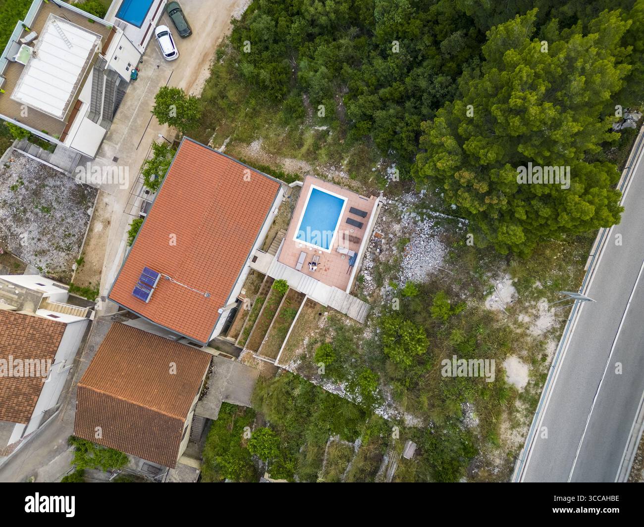 Aus der Vogelperspektive auf die Terrakotta-Dächer treffen auf die türkisfarbene Umarmung eines privaten Pools inmitten von grünen Bäumen, eine sonnenverwöhnte Oase, Drvenik, Kreis Split-Dalmatien, Kroatien. Stockfoto