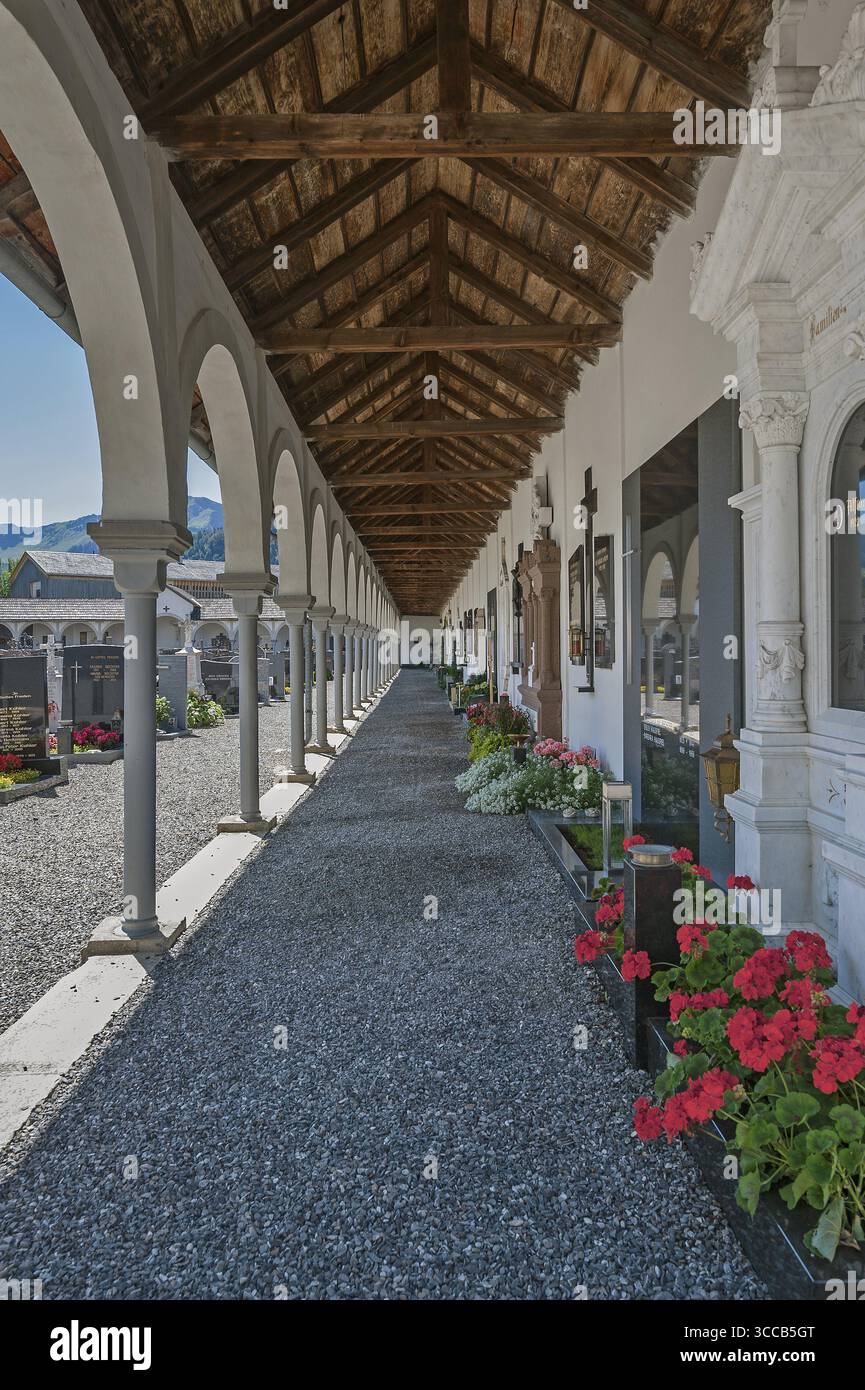 Kreuzgang mit Gräbern und Blumenschmuck auf dem Friedhof der katholischen Pfarrkirche St. drei Könige, Hittisau, Bregenzerwald, Vorarlbe Stockfoto