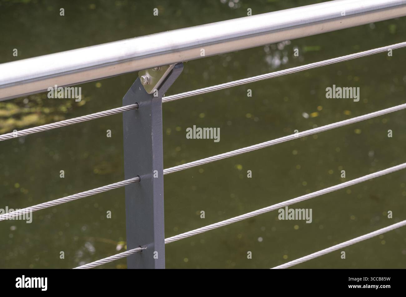 Nahaufnahme eines Stahlseilgeländesystems mit verschwommenem grünem Wasserkörper im Hintergrund Stockfoto