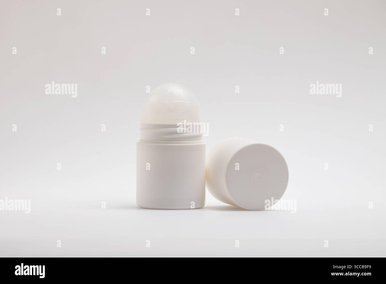 Eine weiße, nicht etikettierte Roll-on-Deodorant-Flasche steht aufrecht neben dem abgenommenen Verschluss, der horizontal auf einem sauberen, Stockfoto