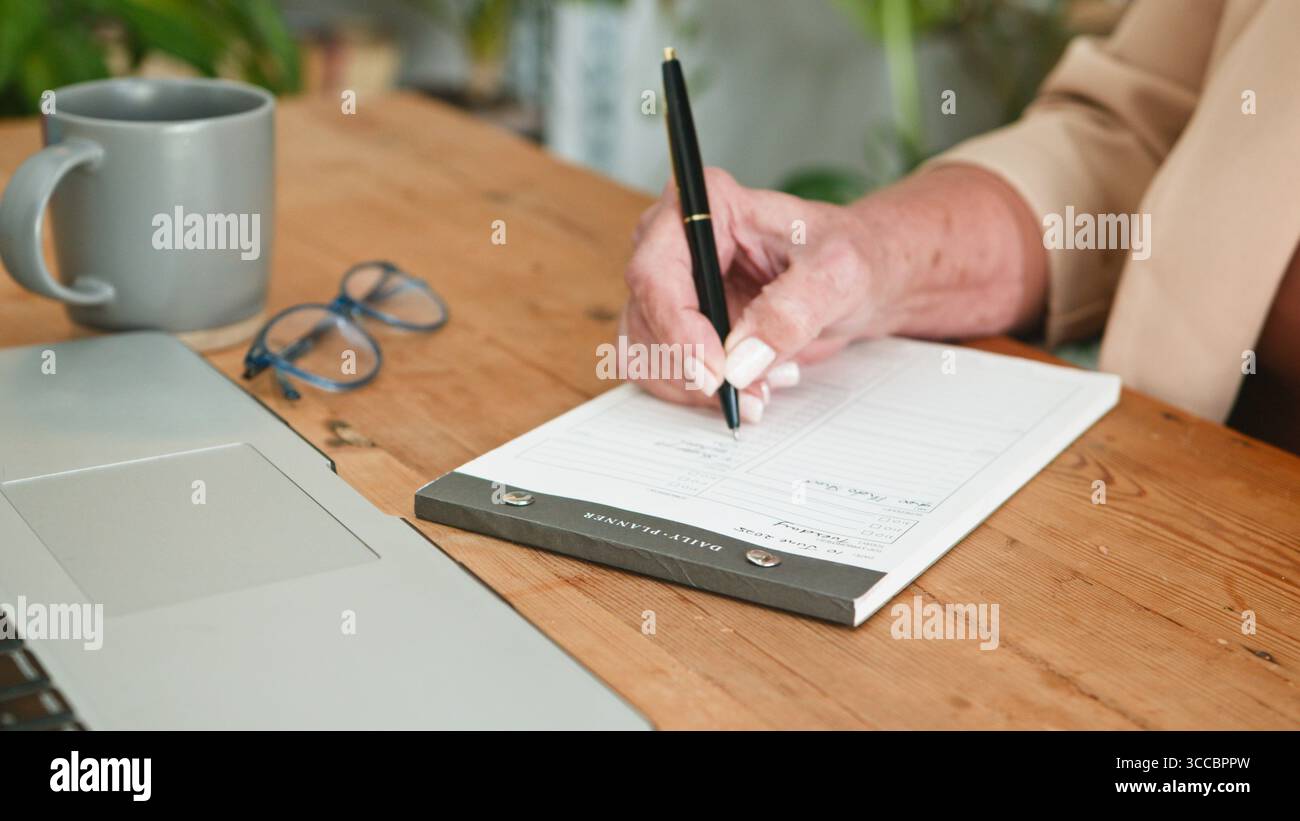 Ältere Frau schreibt Notizen am Schreibtisch im Home Office Workspace Stockfoto
