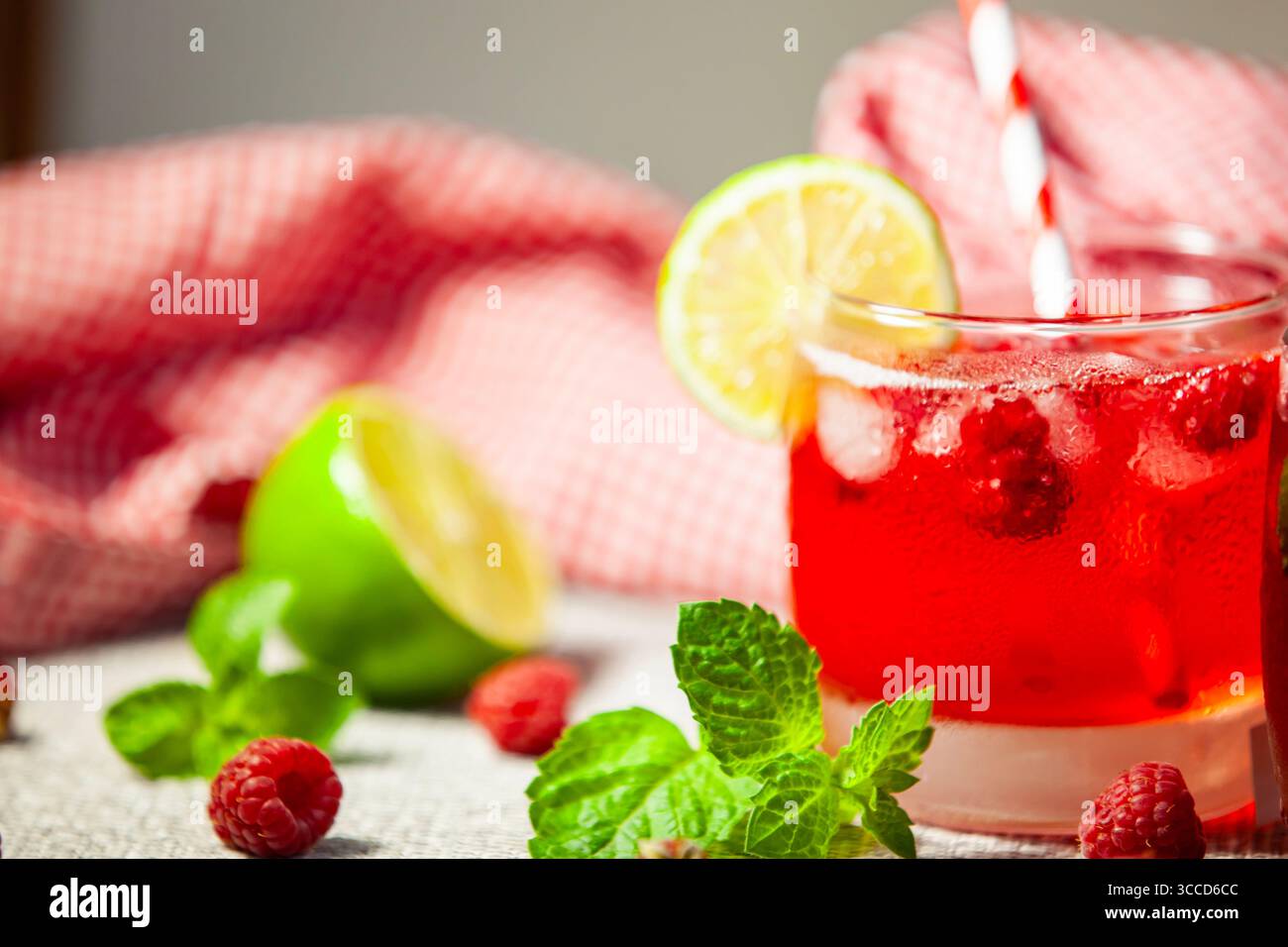 Ein Glas roter Himbeergetränk mit gestreiftem Stroh, Limette und Minze - frischer und verspielter Sommer-Vibe. Stockfoto
