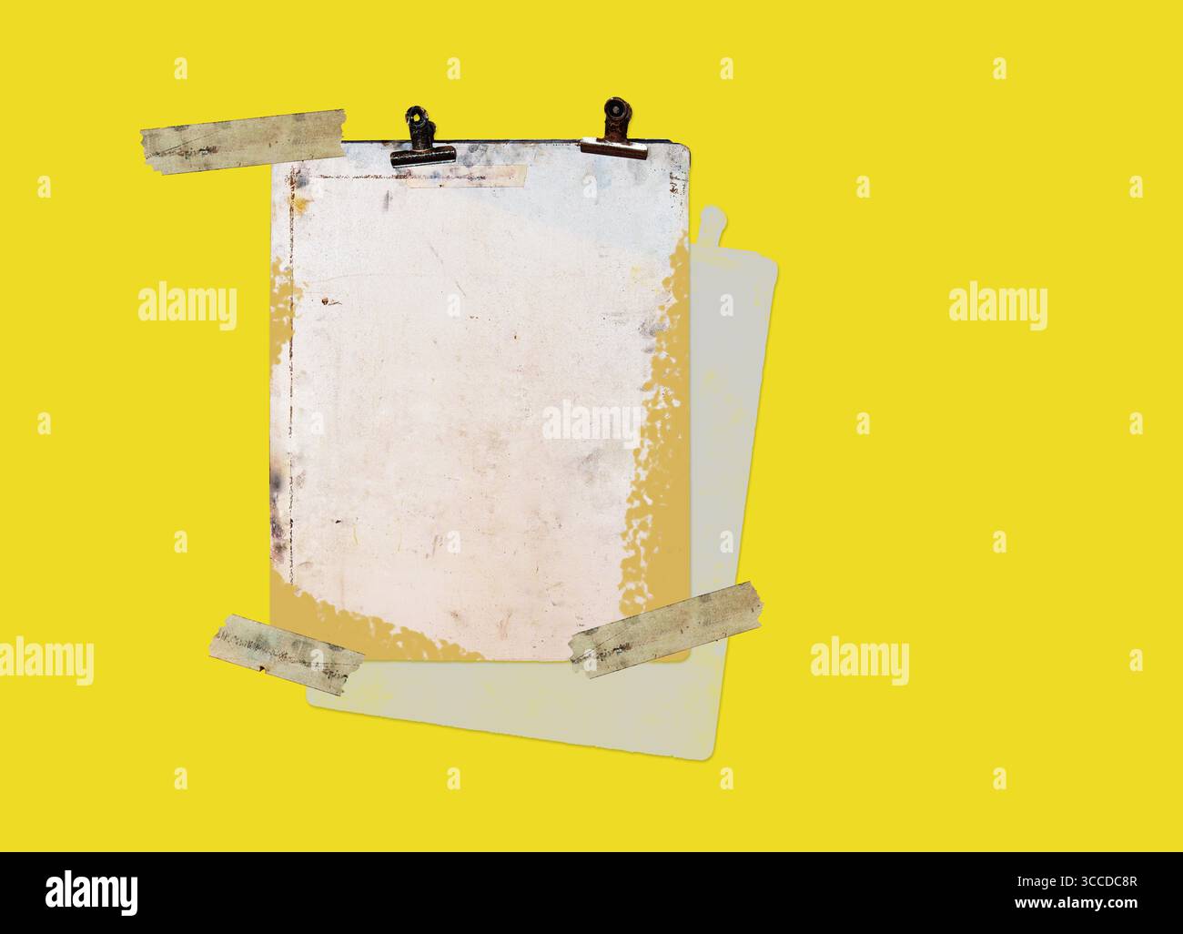 Ein altes, verwittertes Clipboard mit rostigen Clips ist schräg auf gelbem Hintergrund geneigt und durch einen ausdrucksstarken Pinselstrich betont Stockfoto