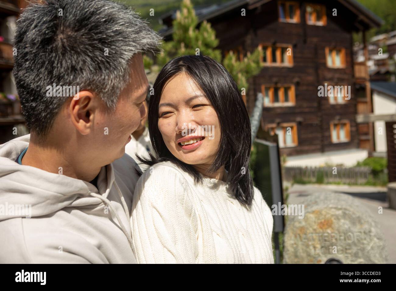 Asiatisches Paar genießt einen romantischen Moment zusammen in einem charmanten Bergdorf mit traditionellen Holzhäusern im Hintergrund Stockfoto