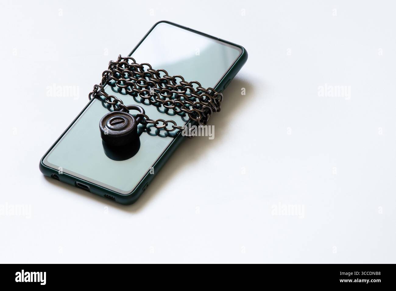 Das Mobiltelefon liegt auf weißem Hintergrund, umwickelt mit einer Metallkette mit einem Schloss für Sicherheit und Datenschutz Stockfoto