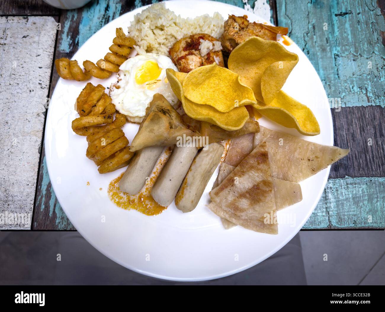 Teller mit Blick von oben mit verschiedenen malaysischen Speisen, einschließlich Reis Ei, Hühnchen, Crackers, Würstchen und frittierten Speisen auf rustikalem Holztisch kuala lumpur malaysia Stockfoto