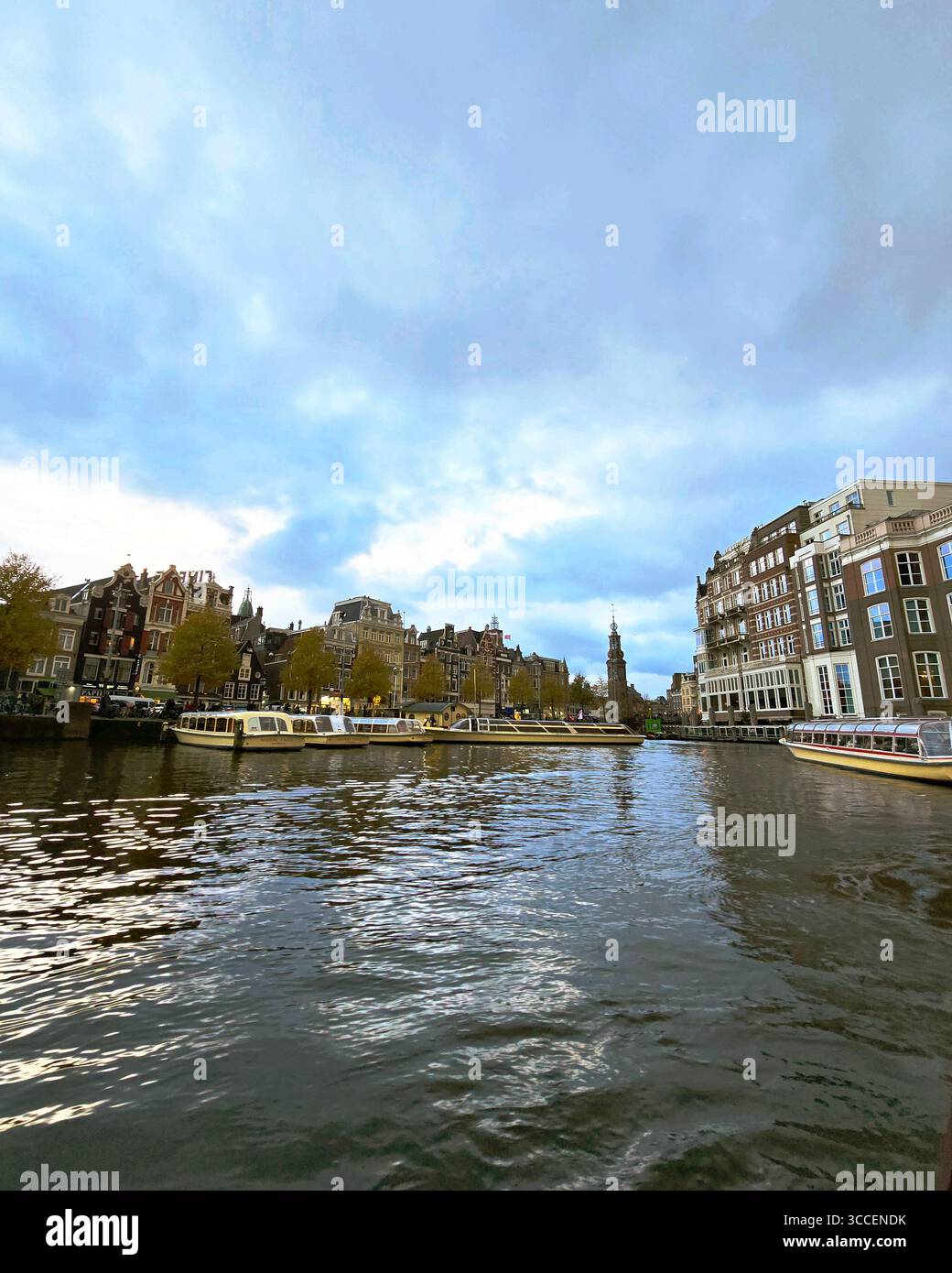 Sonnenuntergang über dem Amsterdamer Hafen mit ruhigem Wasser, das die Lichter und Boote der Stadt reflektiert, Niederlande. - Smartphone-aufgenommenes Stockfoto