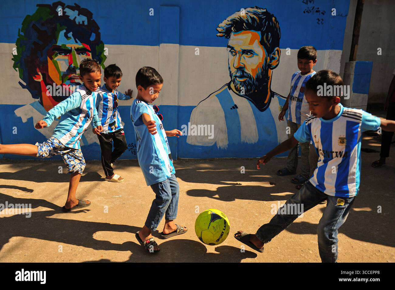 8. Dezember 2022, Sylhet, Bangladesch: Junge argentische Fans spielen Fußball auf den Straßen von Sylhet, wo Graffiti von DIEGO MARADONA aus Argentinien an der Wand gemalt ist. Bangladesch ist ein Land, das sich nie für eine Fußballweltmeisterschaft qualifiziert hat, aber eine große Liebe zum Fußball hat und große Fans sowohl für Argentinien als auch für Brasilien hat. (Bild: © MD Rafayat Haque Khan/ZUMA Press Wire) Stockfoto