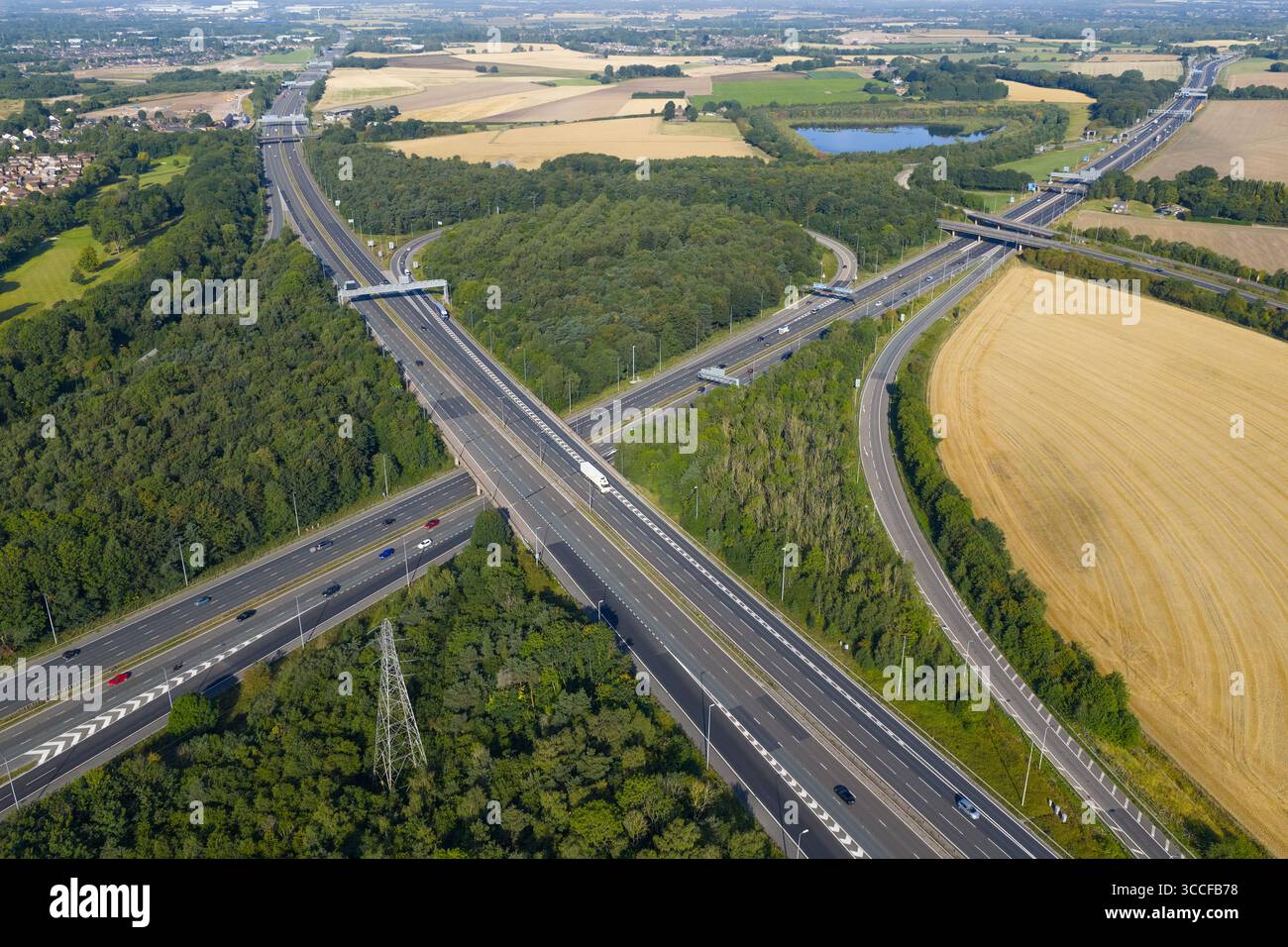 Aus der Vogelperspektive des Croft Interchange (Kreuzung 21A) in der Nähe von Birchwood, wo die Autobahnen M6 und M62 aufeinander treffen, umgeben von Wäldern, goldenem Ackerland und einem sm Stockfoto
