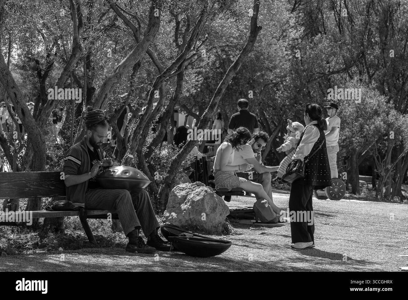 Ein Straßenmusiker spielt eine Blechtrommel auf der Akropolis in Athen, während eine Menschenmenge an einem heißen Sommertag beobachtet, während die Sonne die historische Kulisse der Stadt hervorhebt. Stockfoto
