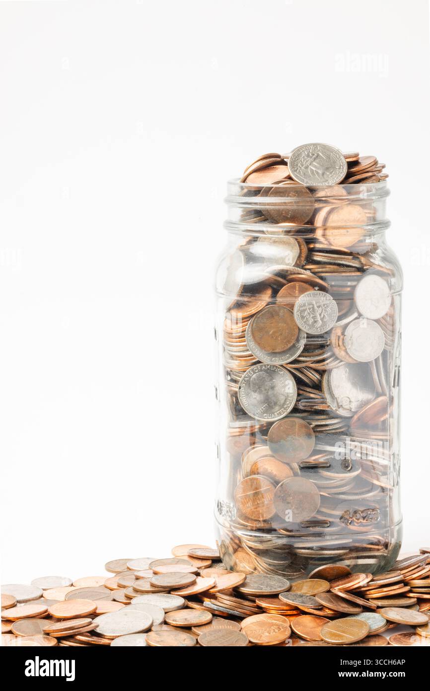 Maurerglas gefüllt mit verschiedenen Münzen auf einem sauberen weißen Hintergrund, das Einsparungen, Budgetierung oder Finanzwachstum symbolisiert. Stockfoto