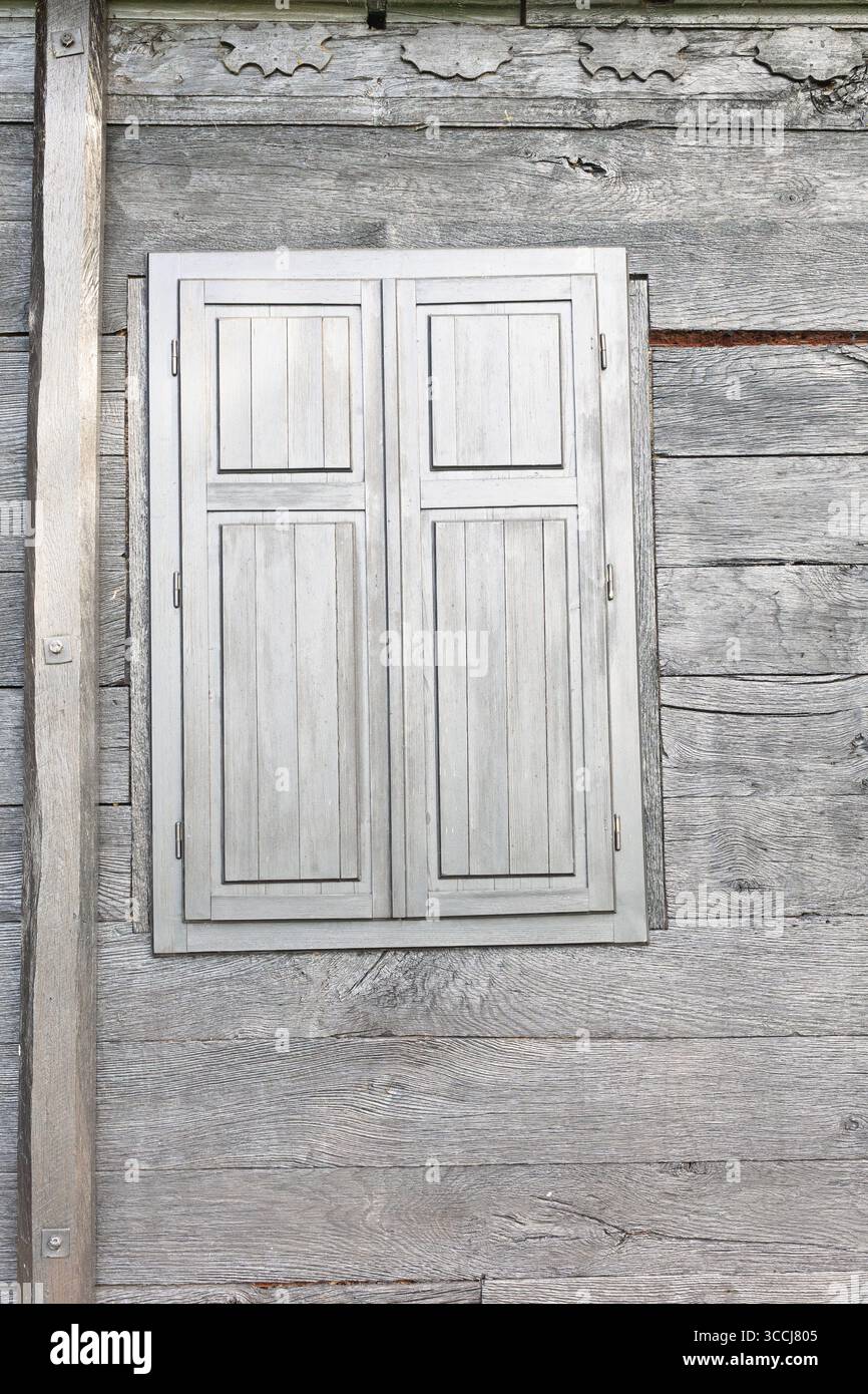 Rustikale Holzwand mit lebendiger Textur und geschlossenen Fensterläden, die charmante Einfachheit und Eleganz der Holzhandwerkskunst hervorheben. Stockfoto