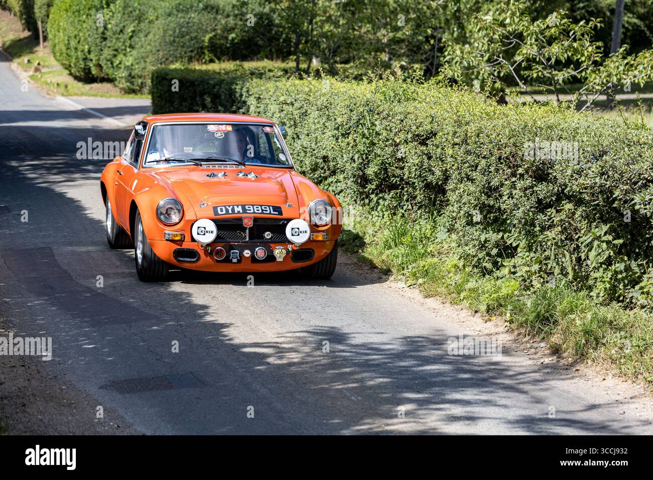 1972 MG B-Sportwagen, der an einem sonnigen Tag auf einer Landstraße fährt, umgeben von Grün und Hecken Stockfoto