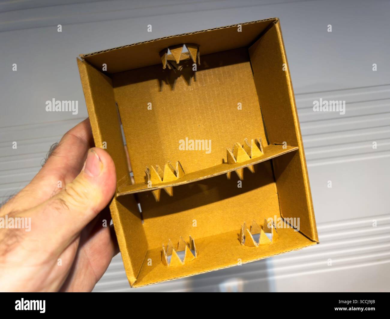 Nahaufnahme eines Trenners aus braunem Wellpappe mit schützenden inneren Spitzen, die von Hand gegen einen neutralen Hintergrund im Innenbereich gehalten werden. Stockfoto