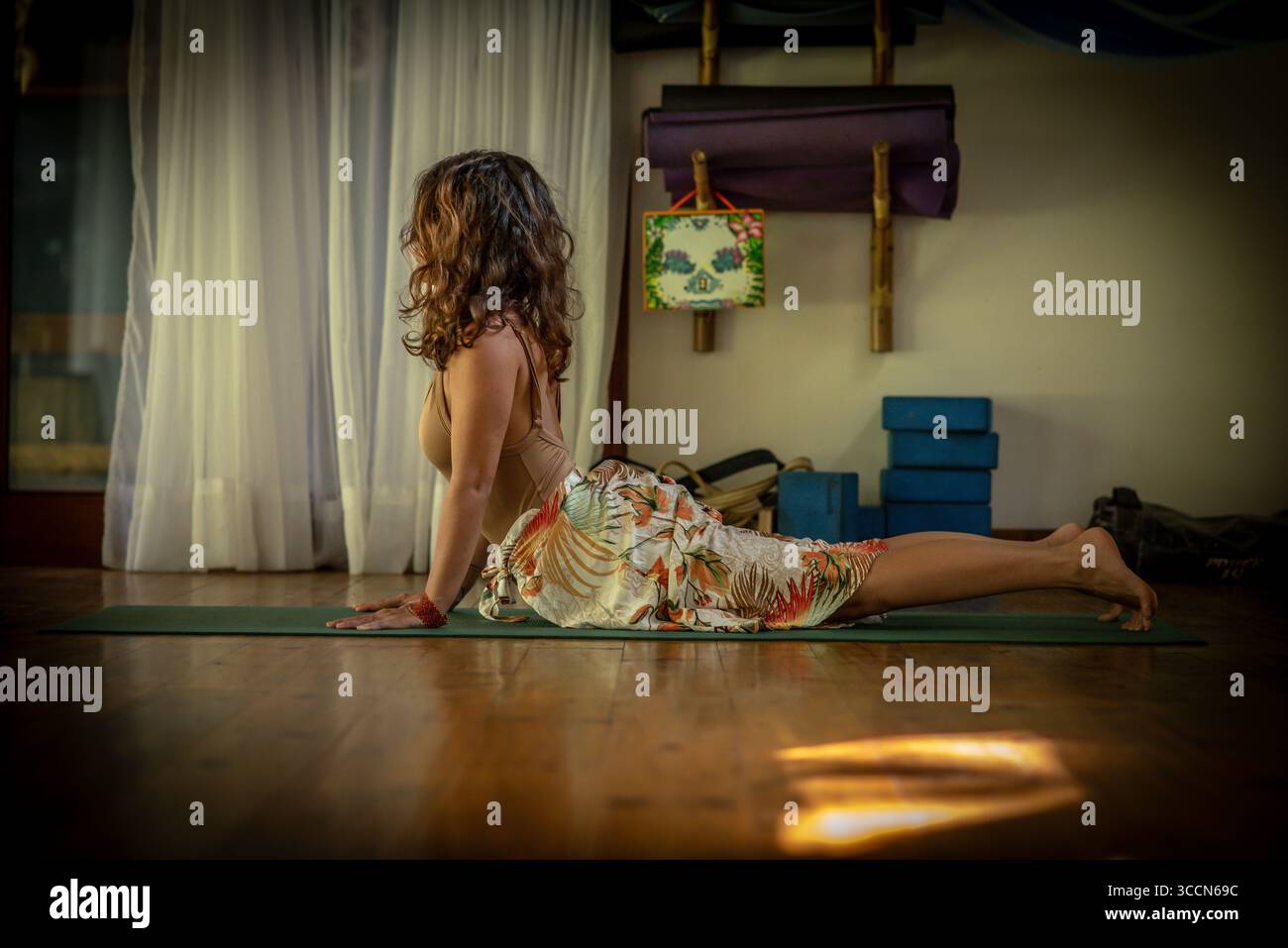 Frau in aufwärts gerichteter Hundestellung während Indoor Yoga-Übungen mit natürlichem Licht und Requisiten Stockfoto