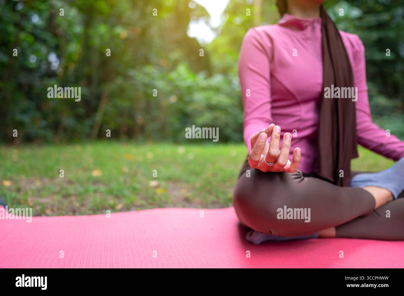 Frau in sportlichem Outfit entspannt sich und meditiert Zen-ähnlich auf einer Fitnessmatte in einem öffentlichen Park im Freien. Konzept eines gesunden aktiven Lebensstils Stockfoto