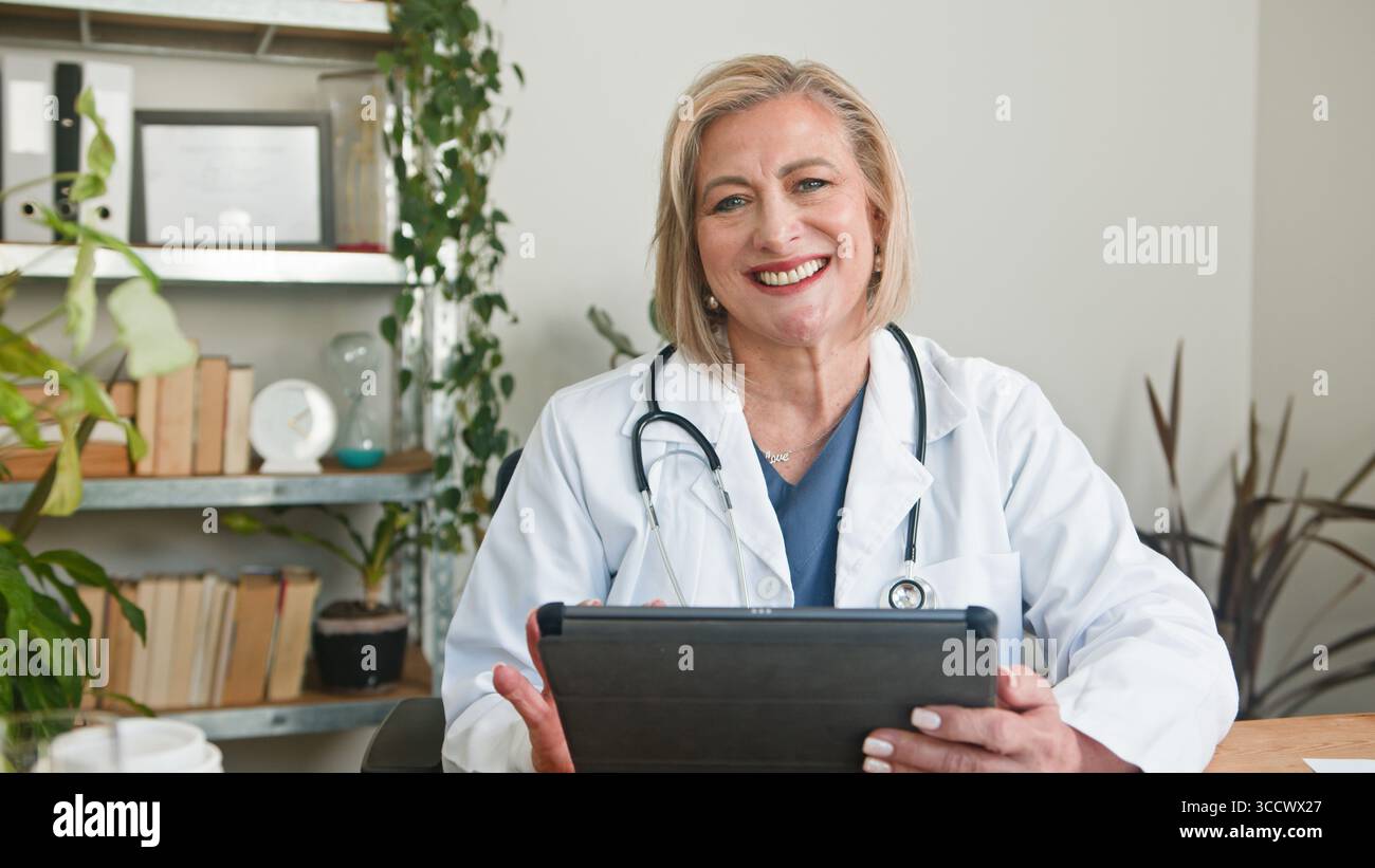 Lächelnder Senior Doctor, der Tablette in der Begrüßungsumgebung des medizinischen Büros hält Stockfoto