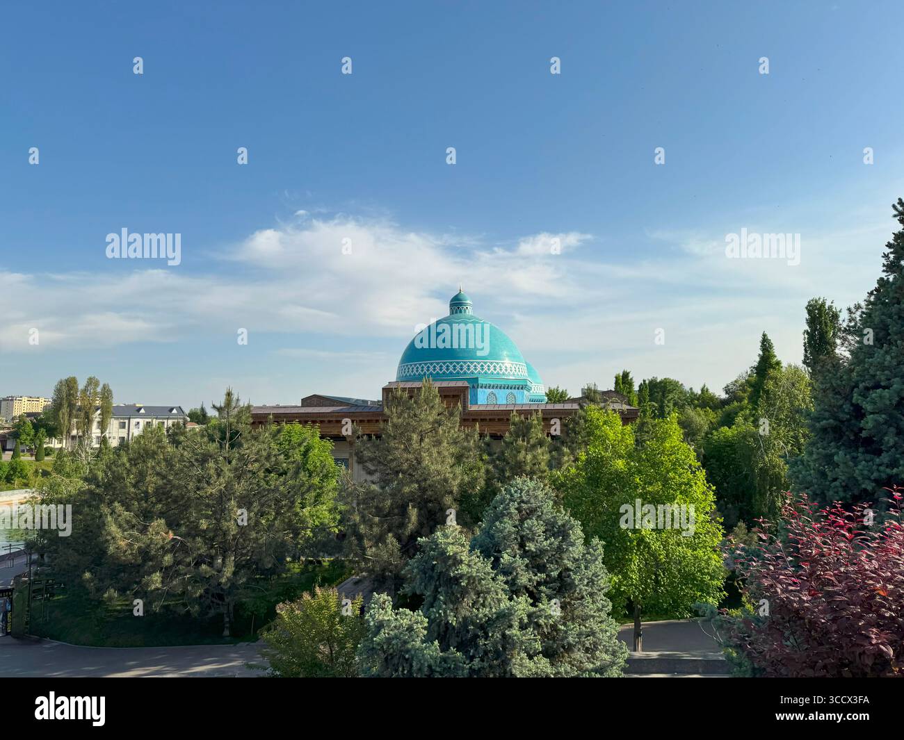 Traditionelle türkisfarbene Kuppel eines Kulturgebäudes, umgeben von grünen Bäumen an einem sonnigen Tag. Gefangen in einer friedlichen Parkumgebung mit klarem blauem SK Stockfoto