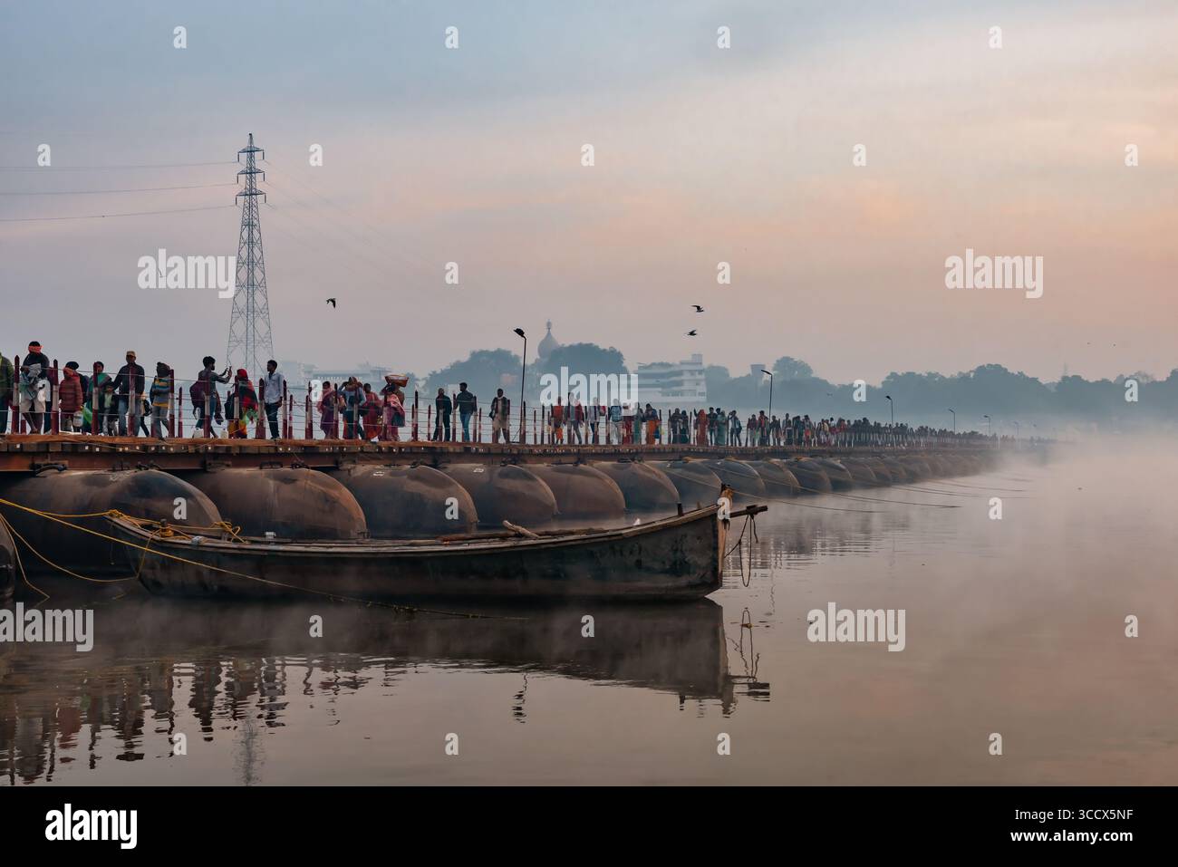 Prayagraj, Indien - 26. Februar 2025: Pilger überqueren eine nebelige Pontonbrücke über den Fluss während Kumbh Mela in Indien, mit sanftem Licht Stockfoto