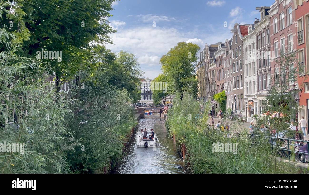 Amsterdam Niederlande 10. August 2025 Ein Boot fährt entlang der schmalen Leliegracht. Die Wände des Kanals wurden durch einen Koffer-Damm verstärkt, der Bereich dazwischen mit Weiden und anderen Bäumen bepflanzt wurde. Achterstallig, onderhoud, Kassettendamm, Reparaturen, wallen Stockfoto
