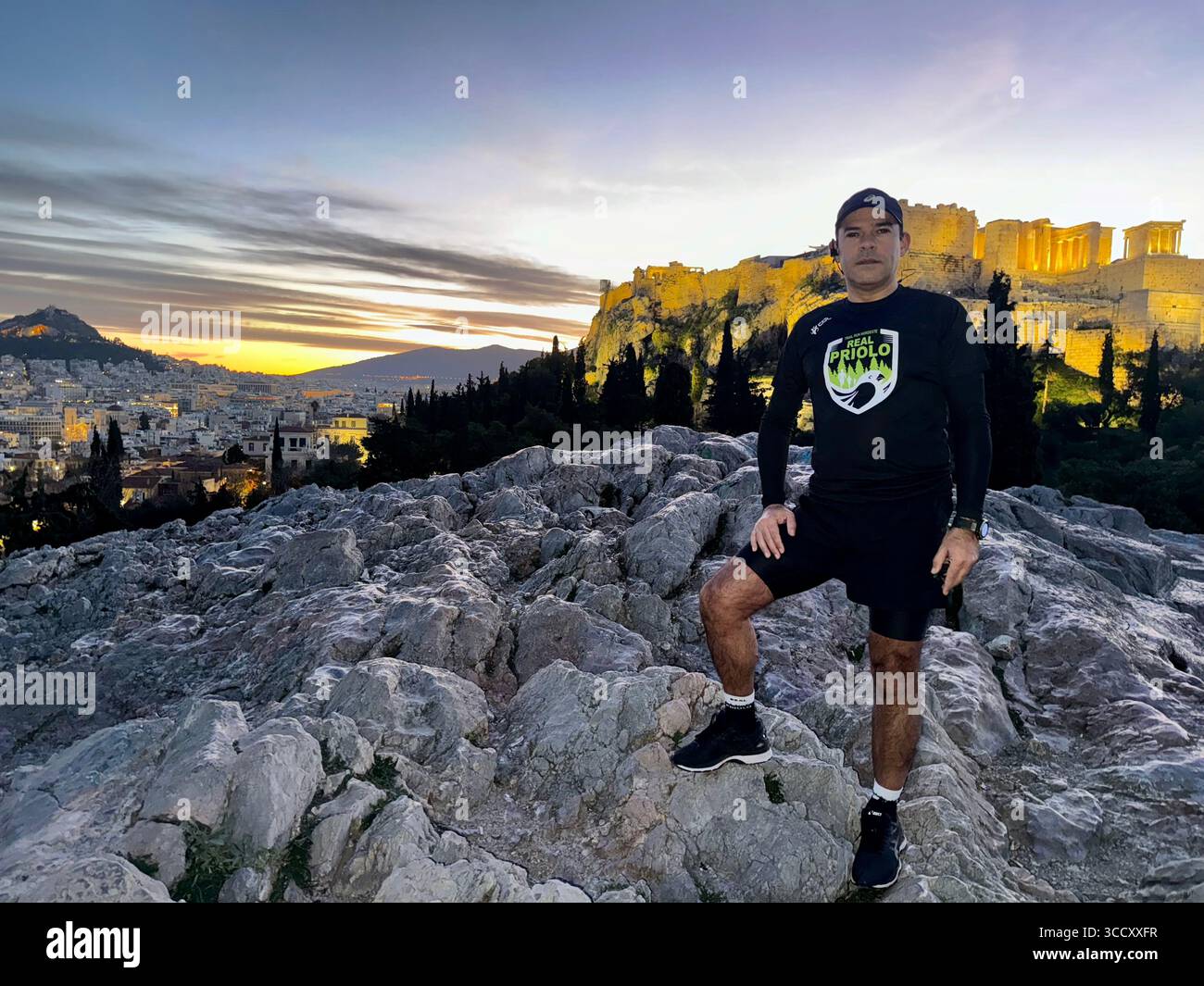Läufer aus Portugal bei Sonnenaufgang am frühen Morgen auf dem Areopagus-Hügel, mit der Akropolis und dem Lycabettus-Hügel im Hintergrund, Athen. - Smartphone-aufgenommenes Stockfoto