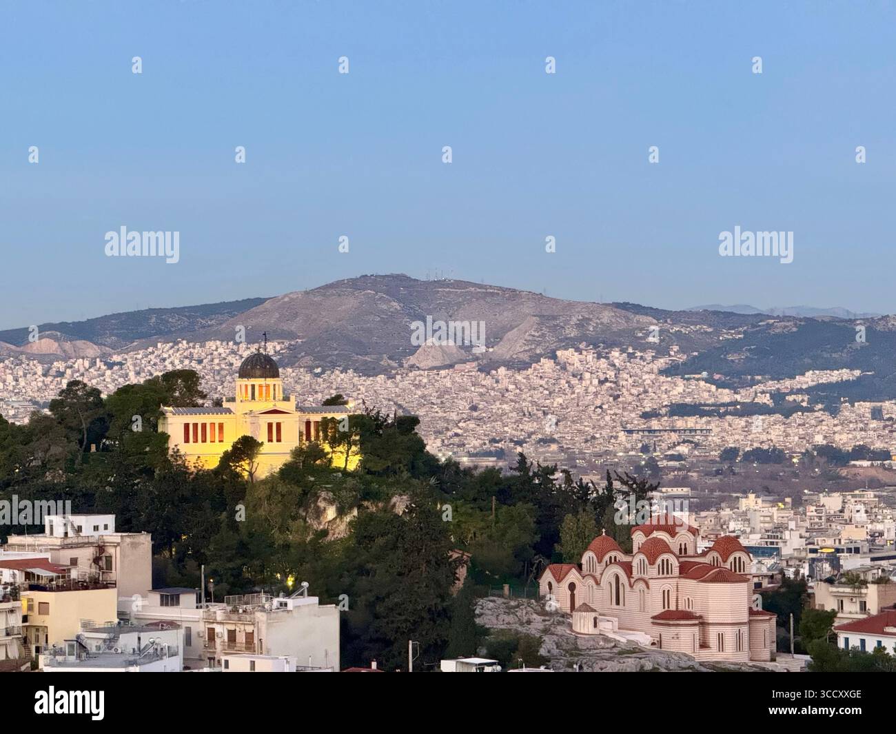 Blick auf den Sonnenaufgang vom Areopagus-Hügel mit dem Stadtbild von Athen, mit dem gelben Gebäude und dem fernen Berg. Stockfoto