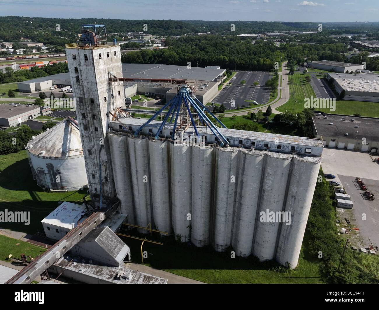 Aus der Vogelperspektive eines hoch aufragenden Getreideaufzugskomplexes, der lange Schatten auf den darunter liegenden Asphalt wirft, im Kontrast zu den grünen Bäumen in der Ferne, Cincinnati, Ohio, USA. Stockfoto