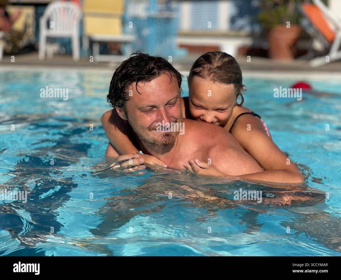 Vater und Tochter genießen spielerische Momente in einem Pool und fangen das Wesen eines fröhlichen Familienerlebnisses im Wasser ein. Sie teilen ein Lächeln und Stockfoto