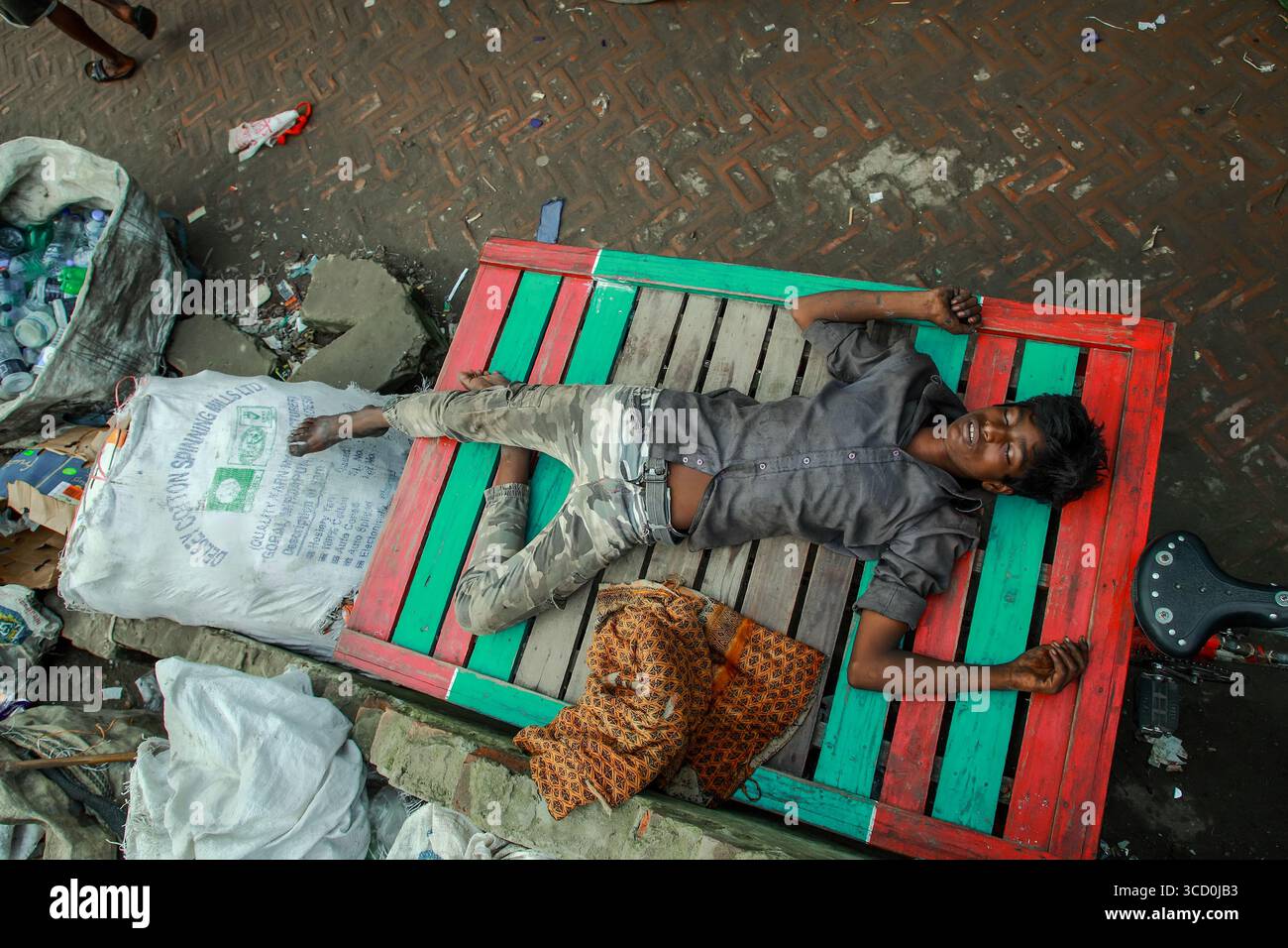 Dhaka, Bangladesch - 15. August 2021: Blick auf einen lächelnden Jungen liegt auf einer lebhaft bemalten Holzpalette inmitten der harten Realität von Abfall und Armut. Stockfoto
