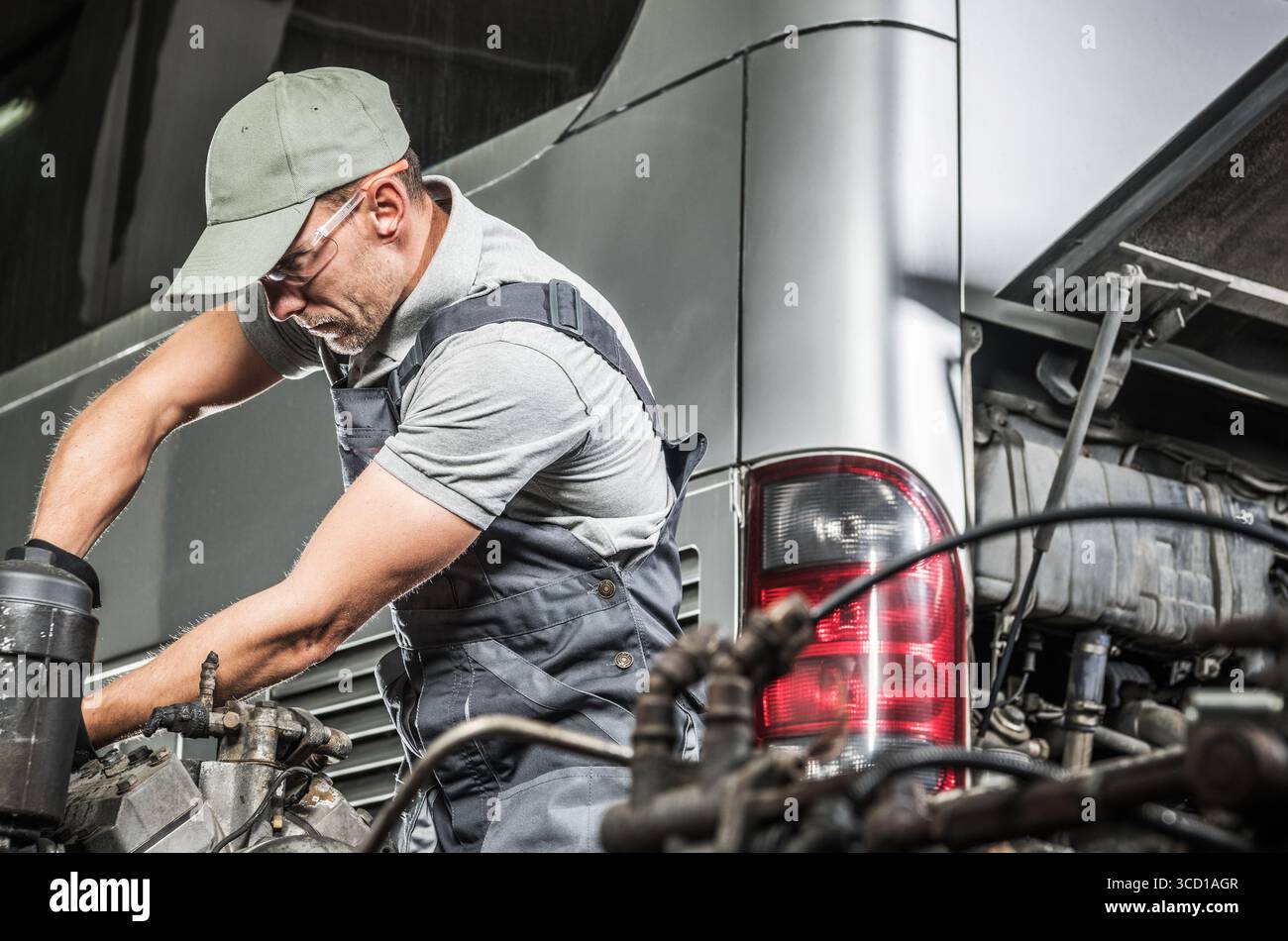 Ein erfahrener Mechaniker arbeitet fleißig an einem Motor in einer hell beleuchteten Werkstatt, umgeben von Werkzeugen und Fahrzeugteilen, um sicherzustellen, dass alles reibungslos läuft Stockfoto