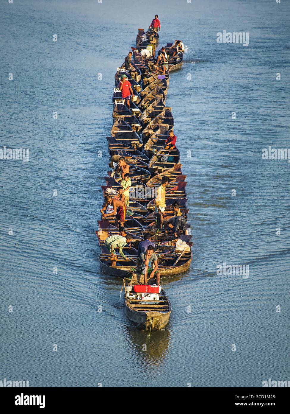 Bogura, Bangladesch - 03. November 2017: Blick auf dicht gepackte Boote, beladen mit Menschen, die einen dunklen Pfad über die glitzernde, sonnengeküsste Flussoberfläche schmieden. Stockfoto