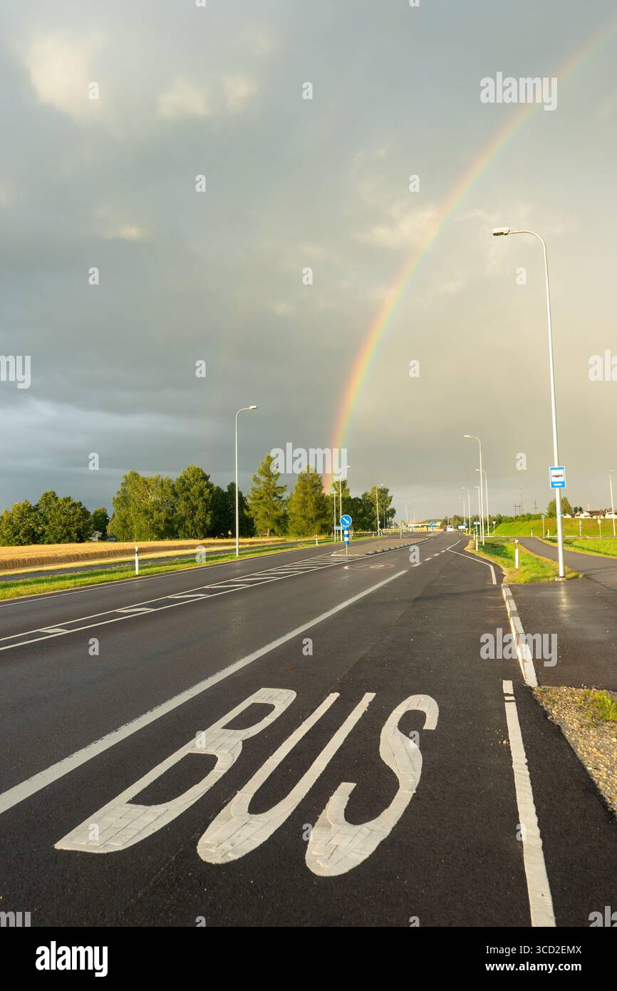 Straße mit Busspurmarkierung unter Regenbogen nach Regen in Estland Stockfoto