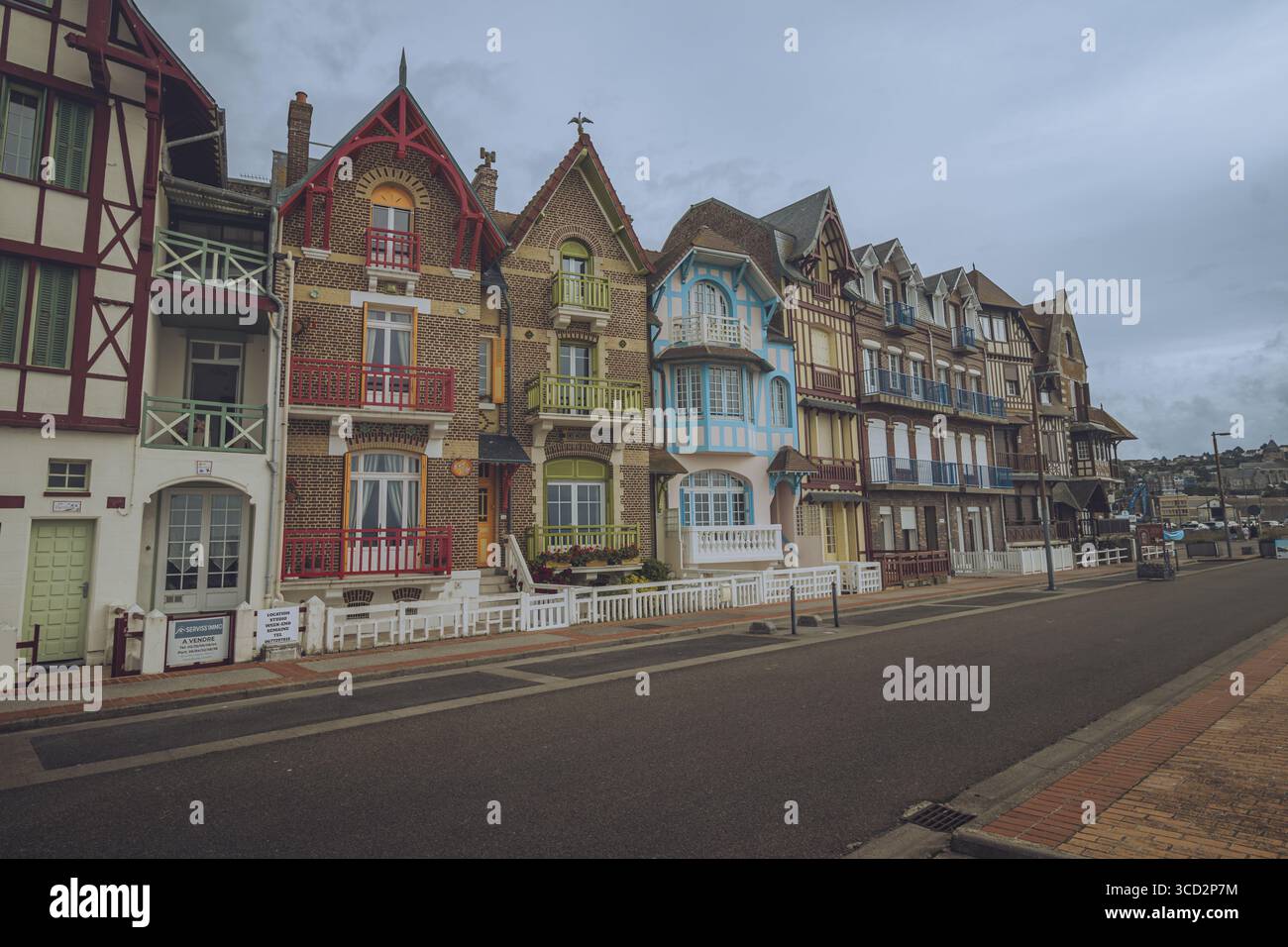 Blick auf eine Reihe lebendiger, historischer Häuser, jedes mit einzigartigen architektonischen Details und farbenfrohen Fassaden, säumen eine ruhige Straße unter einem bewölkten Himmel, Mers-les-Bains, Hauts-de-France, Frankreich. Stockfoto