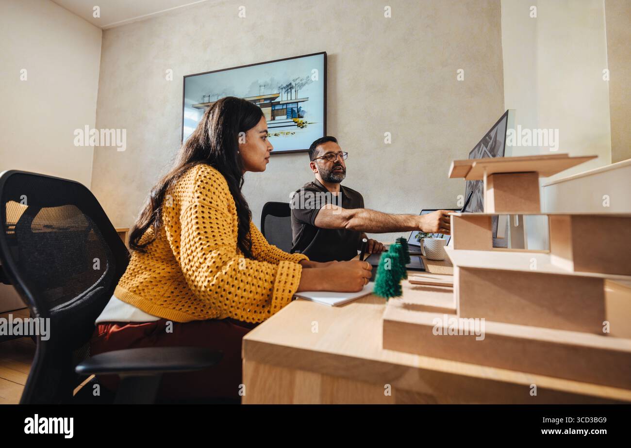 Zwei Personen beteiligten sich an einem Gemeinschaftsprojekt in einem hellen Büro und repräsentieren ein modernes und fokussiertes Architekturbüro. Stockfoto