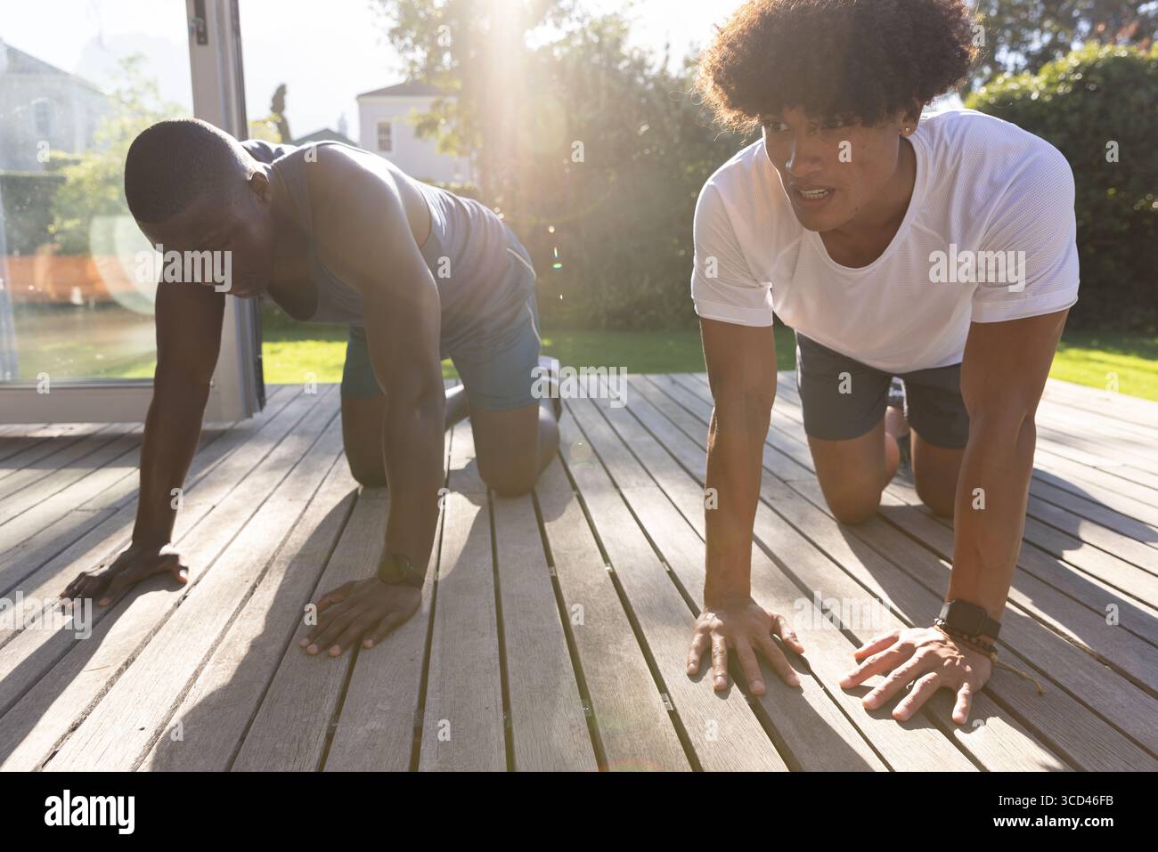 Verschiedene männliche Freunde knieten auf Holzdeck im Garten und dehnten ihre Haltung mit Fitness-Tracker Stockfoto