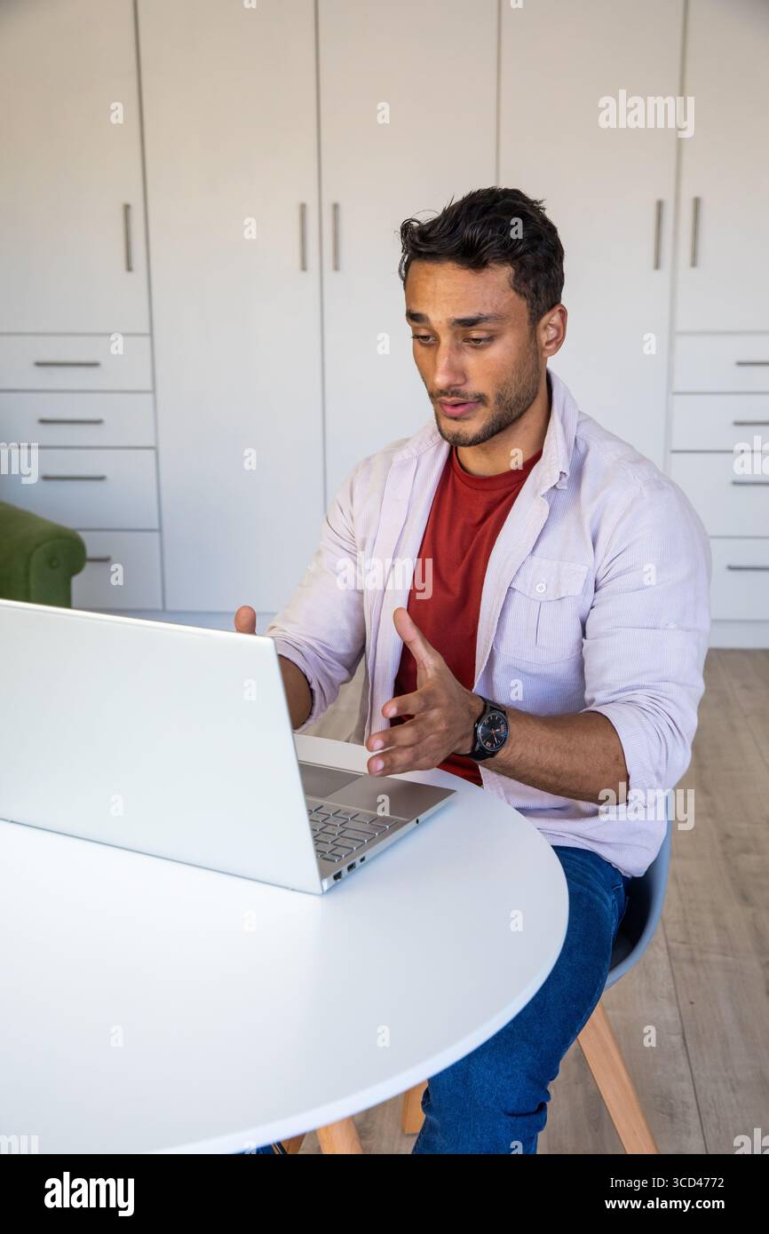 Mann, der während eines Anrufs mit einem Laptop an einem runden weißen Tisch mit einer Armbanduhr gestickt hat Stockfoto