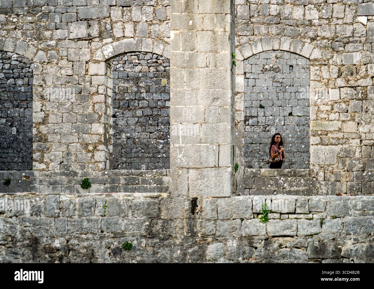 Eine Person, die in der Nähe einer alten Steinmauer mit Bogenfenstern steht. Stockfoto