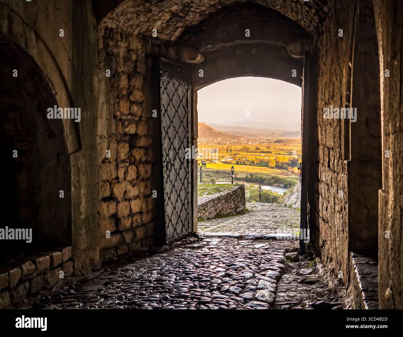 Ein Steinbogen öffnet sich zu einem malerischen Blick auf ein Tal bei Sonnenuntergang. Stockfoto