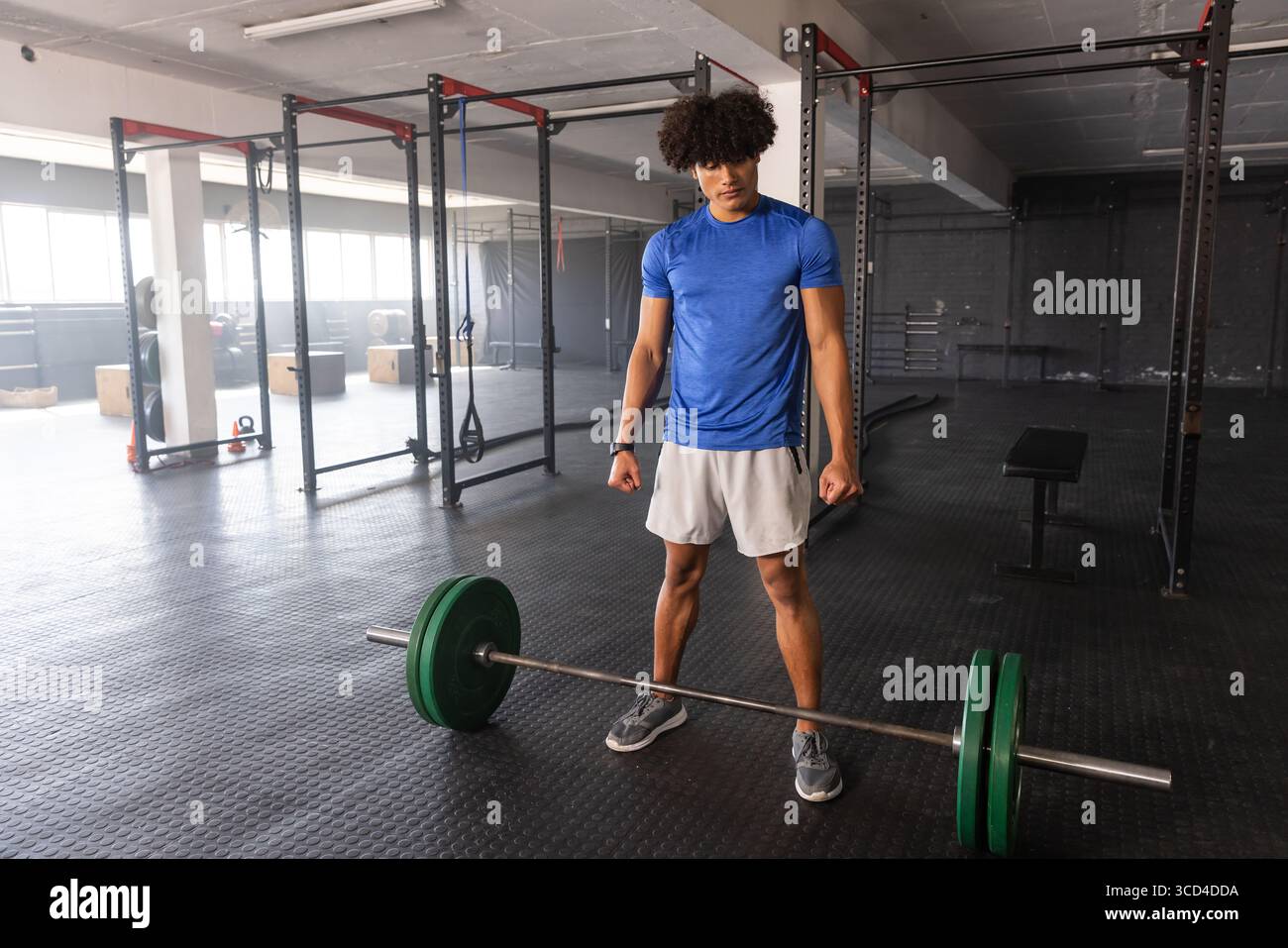 Männlicher Gewichtheber, der sich darauf vorbereitet, beladene Langhantel in der Nähe von Hockregalen anzuheben, flache Bank auf Gummi-Fitnessboden Stockfoto