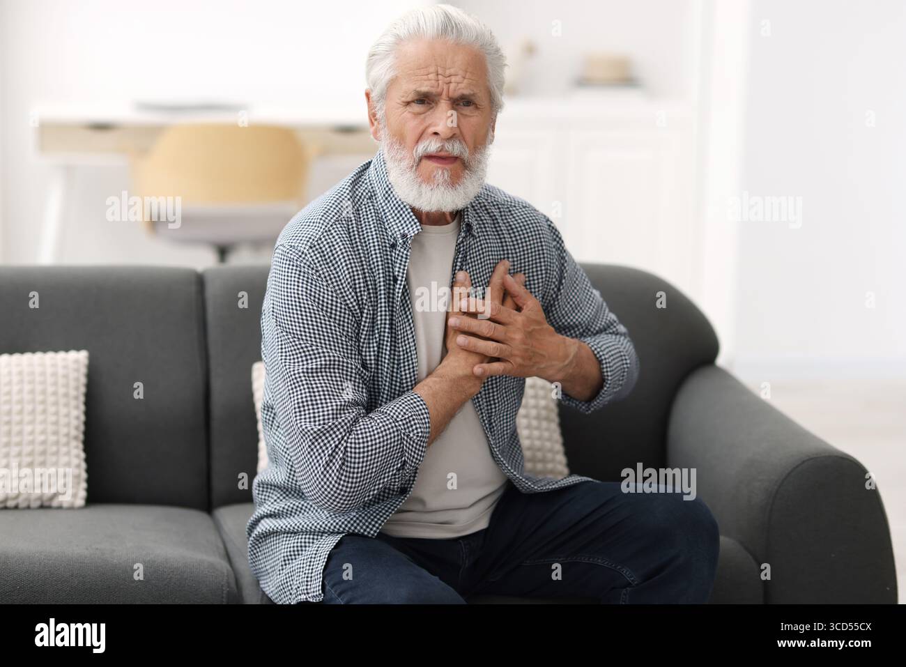 Ein älterer Mann, der zu Hause an Brustschmerzen leidet Stockfoto